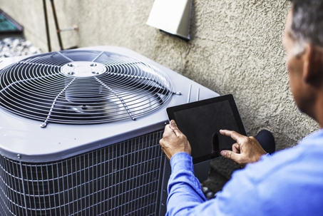 Maintenance engineer using digital tablet to inspect air conditioning unit.